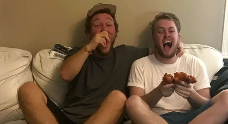 Two men eating and laughing on a couch | Source: AmoMama