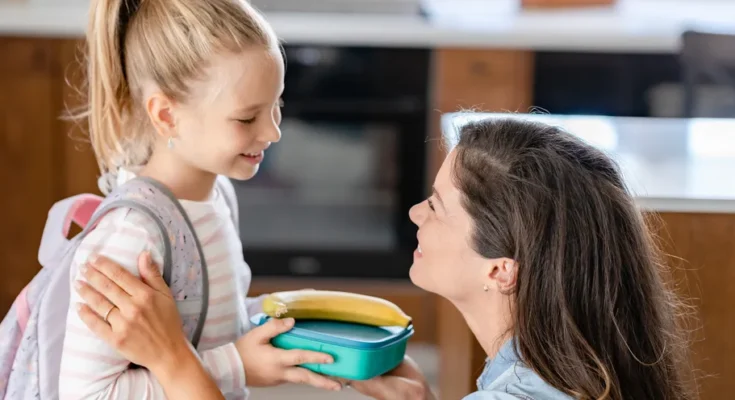 A woman handing a lunchbox to her daughter | Source: Shutterstock