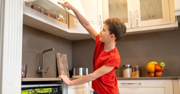 A boy opening a kitchen cupboard | Source: Shutterstock