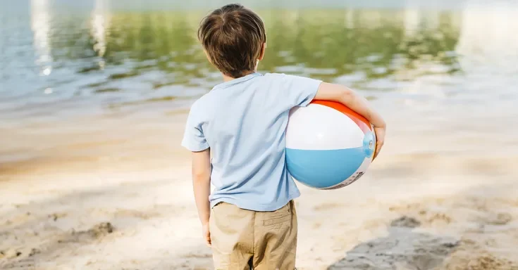 A little boy holding a ball on the beach | Source: Freepik