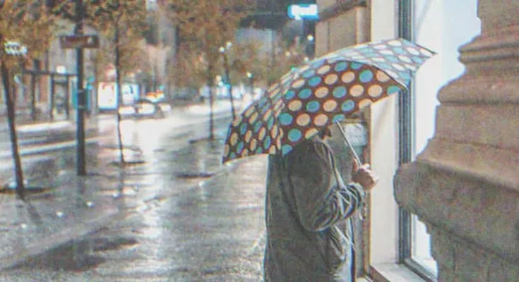 An old lady holding an umbrella and looking inside a business | Source: Shutterstock