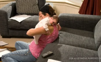 A woman sitting on the floor with her head sunken in one hand while holding a baby over her shoulder | Source: Getty Images