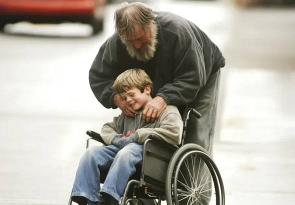 A homeless man leaning over a smiling boy in a wheelchair | Source: Amomama